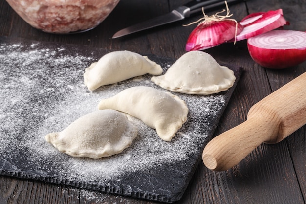 Dumplings raw on a wooden board. Traditional homemade food. The process of cooking dumplings. Traditional pierogi, pelmeni, ravioli, dumplings with meat.