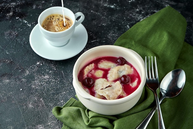 Dumplings with cherries in sauce and with sour cream on a dark background Ukrainian dessert varenyky