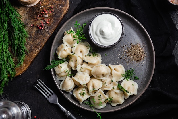 Photo dumplings with sour cream and herbs on a dark plate meat dumplings