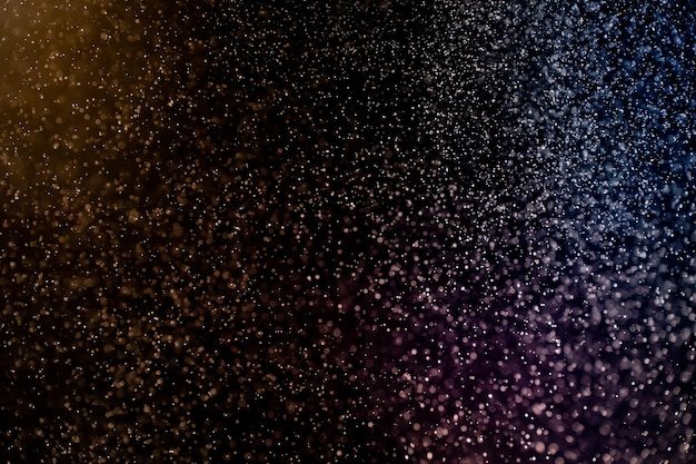 Dust particles floating on a colorful rainbow light on black background. Glittering sparkling.