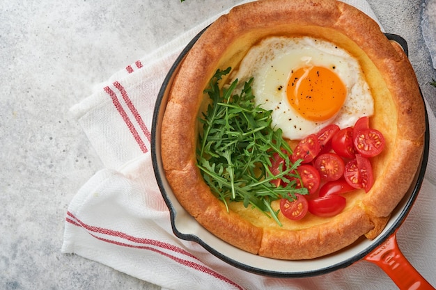 Dutch baby pancake Fresh homemade Dutch Baby pancake with fried egg tomato and green arugula in reed castiron pan on light gray concrete rustic table Flat lay close up