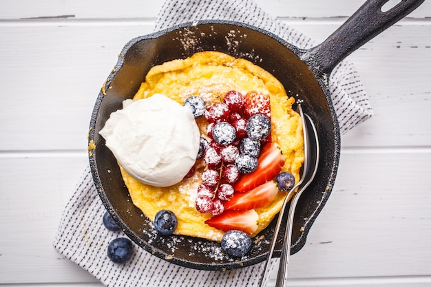 Dutch baby pancake with berries in a cast-iron pan on a white background.