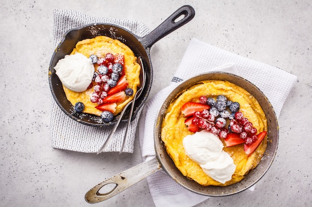 Dutch baby pancake with berries and cream in a cast-iron pan, top view.