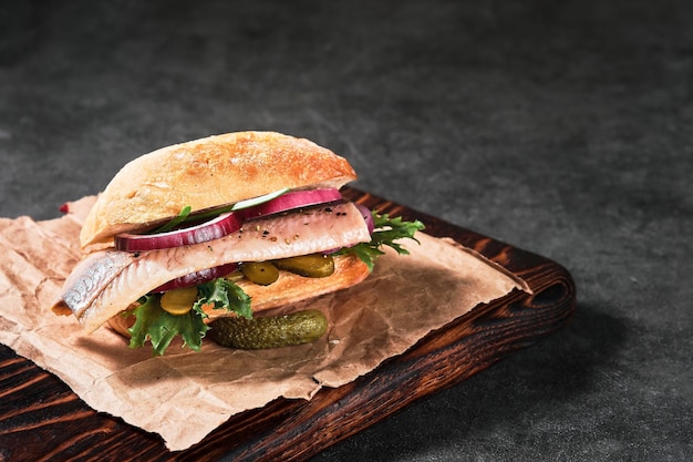 Dutch sandwich with herring and pickles cucumber and red onion on the gray table. Close up, selective focus and copy space