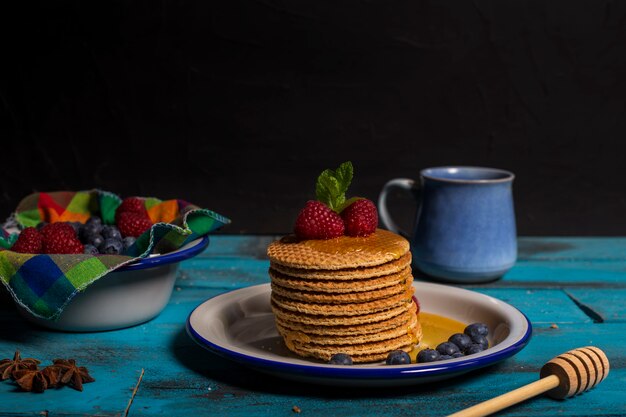 Dutch waffle breakfast with raspberry, blueberry and honey with anise leaves on blue wooden background. Isolated image Front image. Breakfast concept.