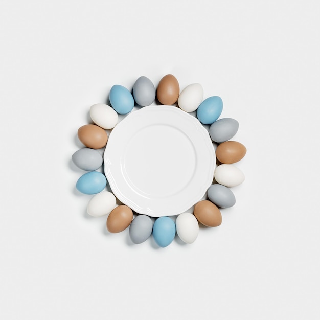 Dyed Easter eggs beige gray blue colors around white plate light background with empty plate and