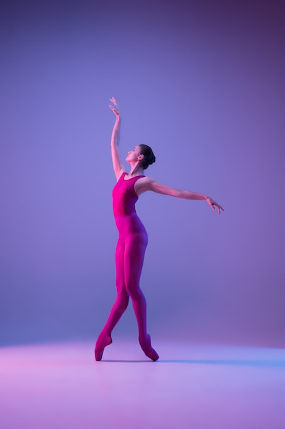 Dynamic. Young and graceful ballet dancer isolated on purple studio background in neon light. Art, motion, action, flexibility, inspiration concept. Flexible caucasian ballet dancer, weightless jumps.