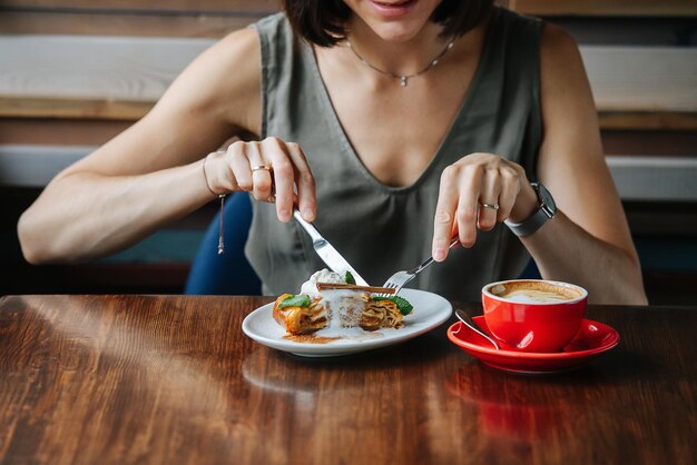 Eager woman eating a pie topped with icecream with fork and knife no face