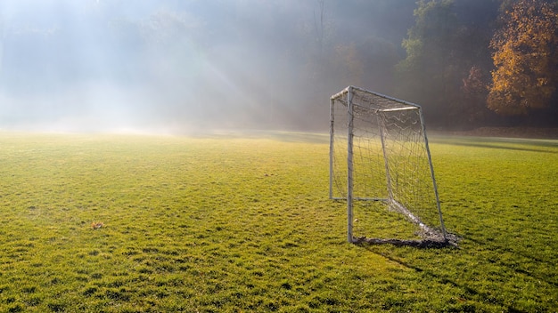 Early morning in the amateur soccer field. Football game playground in autumn foggy morning.