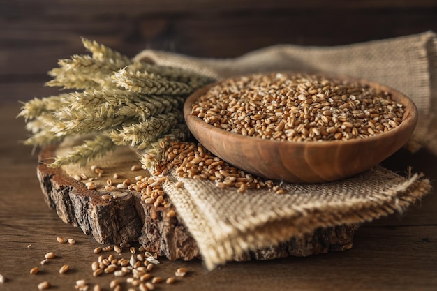 Ears of wheat and bowl of wheat grains on brown wooden background