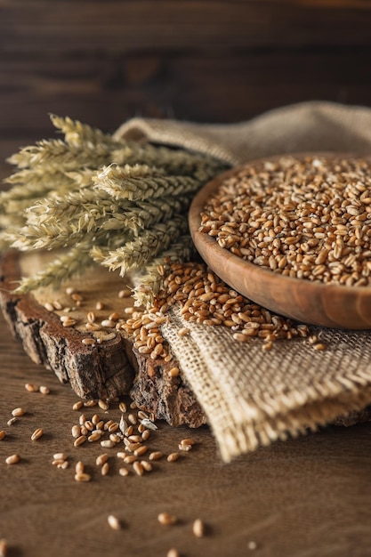 Ears of wheat and bowl of wheat grains on brown wooden background