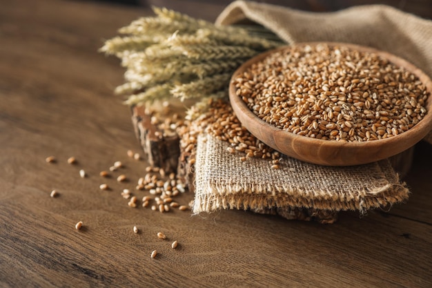 Ears of wheat and bowl of wheat grains on brown wooden background