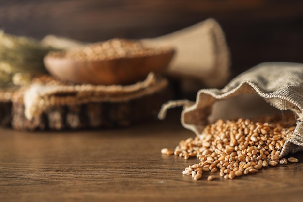 Ears of wheat and bowl of wheat grains on brown wooden background