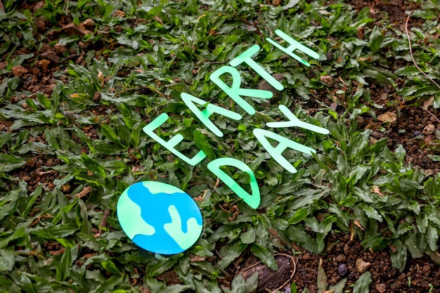 earth day lettering with world globe over natural green grass background.