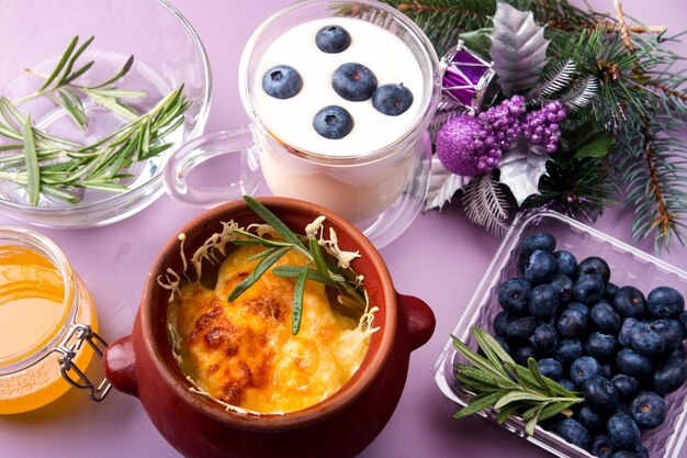 Earthenware pot with baked potatoes and baked cheese A cup of milk with blueberries and a jar of honey