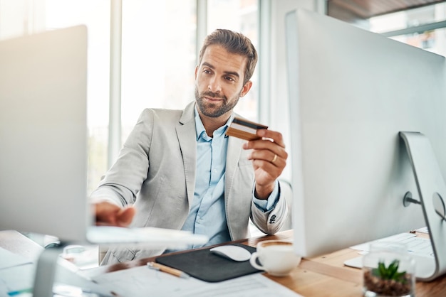 The ease of online banking Shot of a handsome young businessman using a computer while holding a credit card in an office