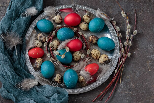 Easter background : on a silver plate, painted eggs (red, blue and quail), feathers and willows