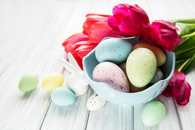 Easter background with colorful eggs in bowl and pink tulips on a white wooden background Top view with copy space