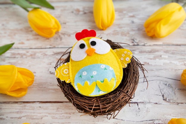 easter background with a decorative chick in a nest surrounded by yellow tulips on a wooden