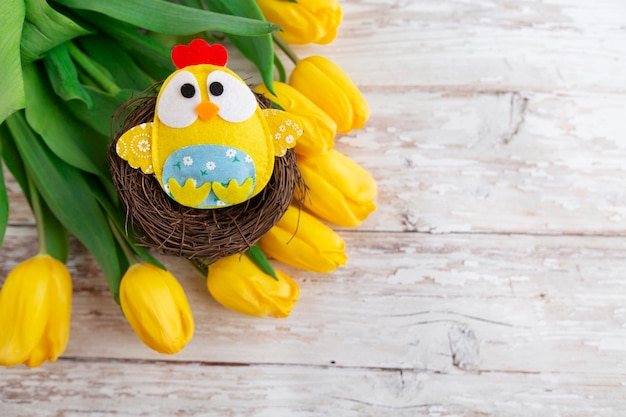 easter background with decorative chicken in nest and yellow tulips on wooden background