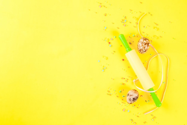 Easter background with quail eggs rolling pin and sugar sprinkling on yellow background Spring holidays concept