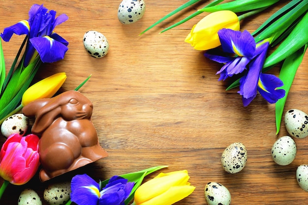 Easter background with a traditional treat chocolate bunny and spring flowers on wooden background, view from above, space for a text