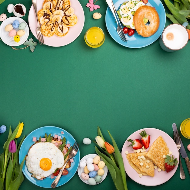 Easter breakfast flat lay with scrambled eggs bagels, tulips, pancakes, bread toast with fried egg and green asparagus, colored quail eggs and spring holidays decorations. Top view. Copy space