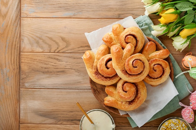 Easter breakfast Holliday concept Easter bunny buns rolls with cinnamon made from yeast dough with orange glaze easter decorations colored eggs on old wooden background Easter Holliday card