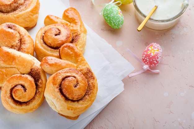 Easter breakfast Holliday concept Easter bunny buns rolls with cinnamon made from yeast dough with orange glaze easter decorations colored eggs on pink spring background Easter Holliday card