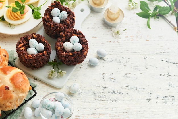 Easter brunch or breakfast Easter chocolate nest cake with chocolate candy eggs traditional hot cross buns and deviled eggs with bouquets of blooming apple trees Spring Easter holiday food concept