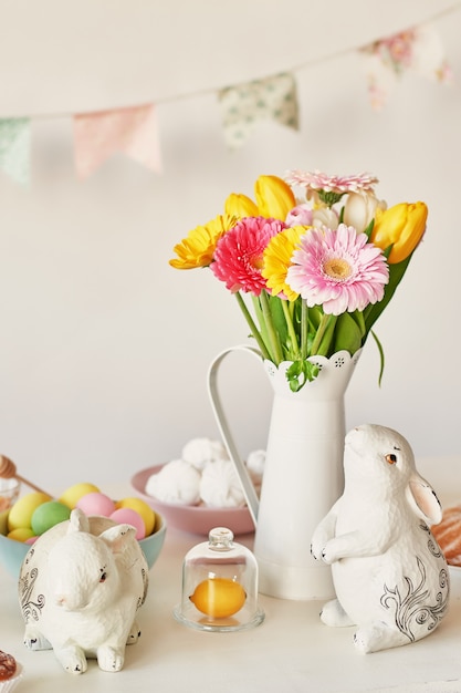 Easter bunny and easter eggs on kitchen table. White rabbit sitting on table with bouquet of tulips and ridge and colorful eggs. Easter decoration with rabbit and eggs. easter card template