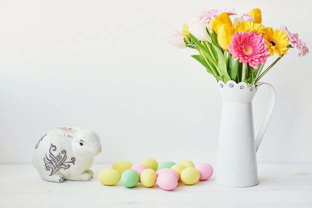 Easter bunny and easter eggs on kitchen table. White rabbit sitting on table with bouquet of tulips and ridge and colorful eggs.