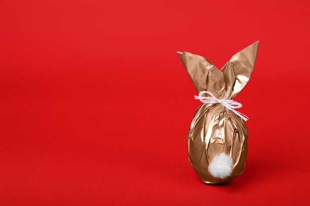 Easter bunny made of shiny gold paper and egg on red background Space for text