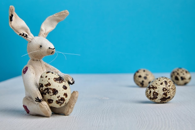 Easter Bunny with spotted quail eggs on a white wooden table on a blue background Easter festive background