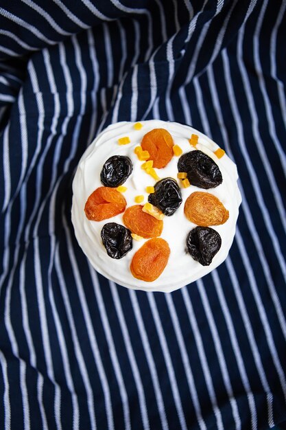 An Easter cake decorated with dried apricots and prunes stands on a blue striped apron. Easter religious holiday concept, top view.