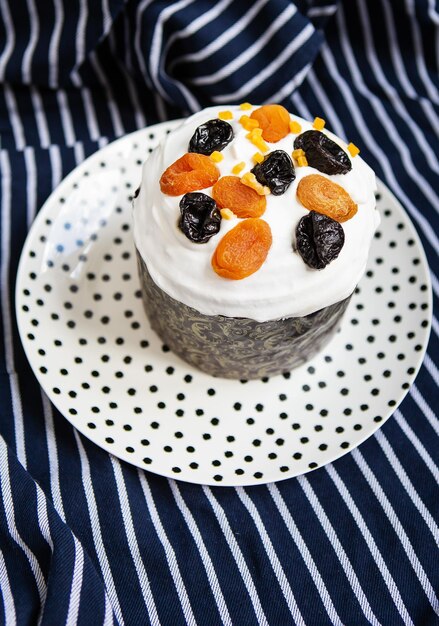 An Easter cake decorated with dried apricots and prunes stands on a plate and a striped blue apron Easter religious holiday concept