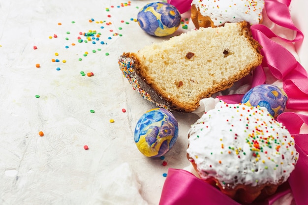 Easter cake and one piece, pink ribbon, colorful sweets on a light background.