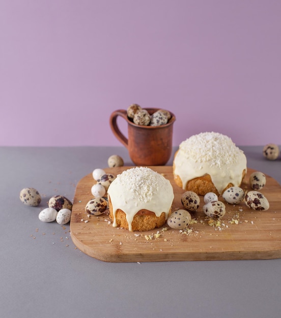 Easter cakes covered with white glaze quail eggs on a wooden cutting board side view easter still life