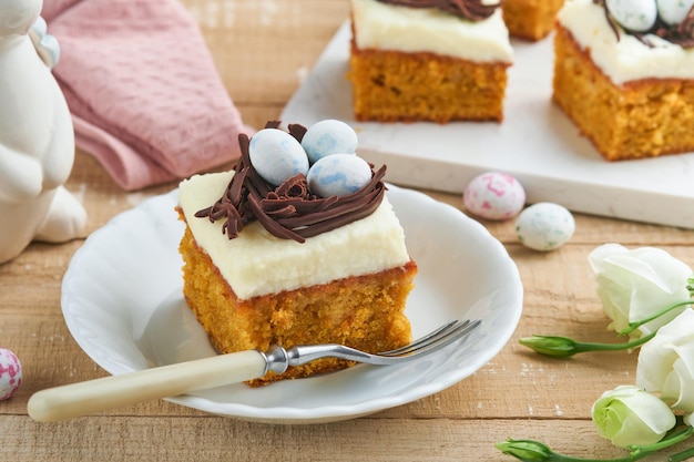 Easter carrot cake bars decorated with chocolate nest and chocolate candy eggs blossoming cherry or apple flowers on rustic light wooden backgrounds Easter holiday meal Traditional Easter food