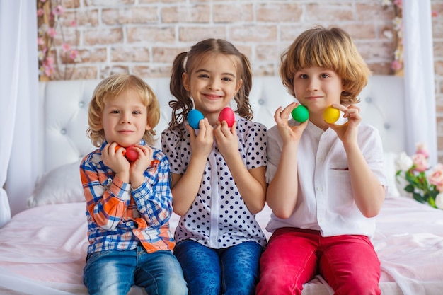 Easter children portrait, funny emotions, surprise. Children, a girl and two boys hold Easter eggs in their hands. Funny photo. Adorable kid in colored clothes enjoying holiday