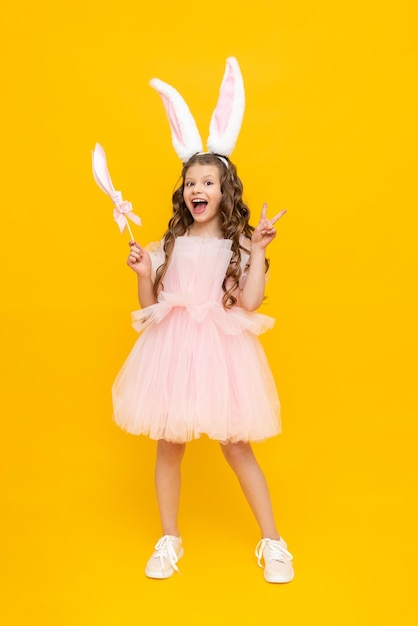 Easter children's holiday A teenage girl in a lush dress rejoices in spring The child is wearing long rabbit ears A beautiful little girl with long hair fulllength on a yellow isolated background