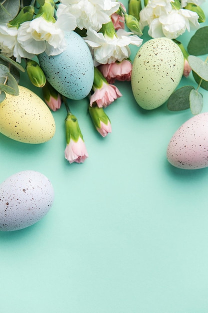 Easter colored eggs and a bouquet of white and pink carnations with eucalyptus branches on a soft green background