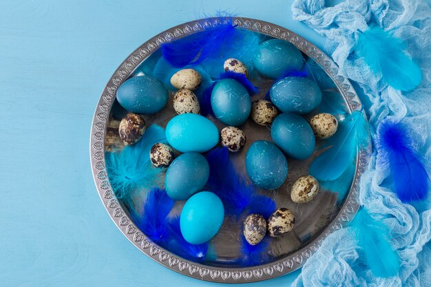 Easter composition: in a blue plate lay blue eggs, quail eggs and feathers