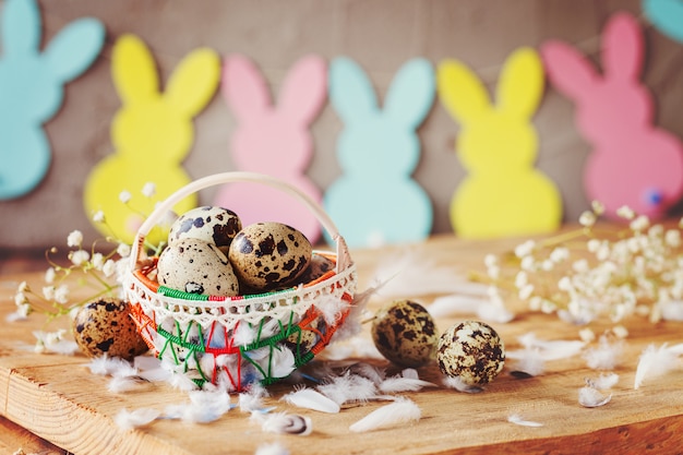 Easter composition of Easter quail eggs in the basket and with bunny garland on wooden