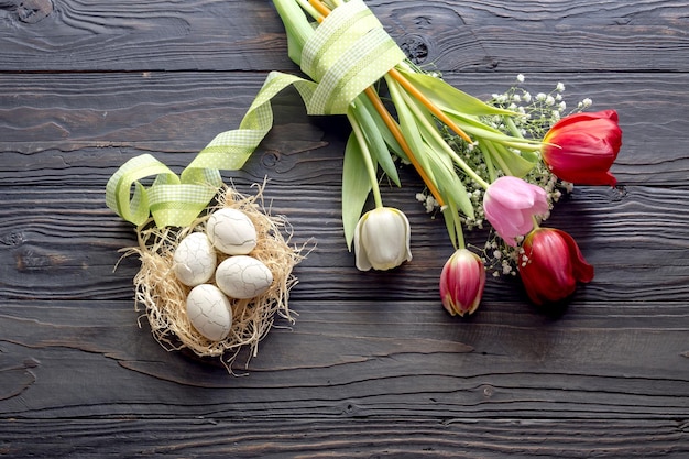 The easter composition Eggs a bouquet of tulips and church candles on wooden table closeup