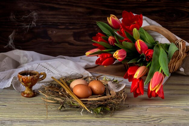 The easter composition Eggs a red tulips censer and church candles on wooden table closeup