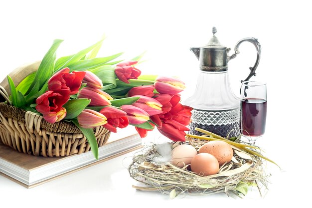 The easter composition Eggs a red tulips church candles and wine in a glass and a jug on white background closeup