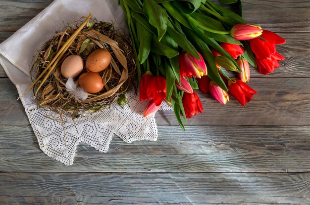 The easter composition Eggs a red tulips and church candles on wooden table closeup