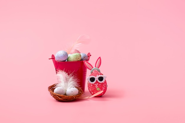 Easter composition on a pink background, a bucket and a nest with eggs close up with copy space