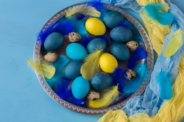 Easter composition: in a silver plate lay blue eggs, yellow eggs, quail eggs and feathers